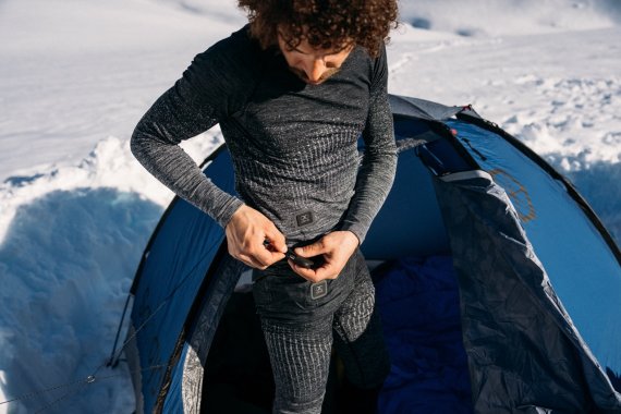 Ein Mann steht vor seinem Zelt in Schnee, gekleidet in Funktionsunterwäsche